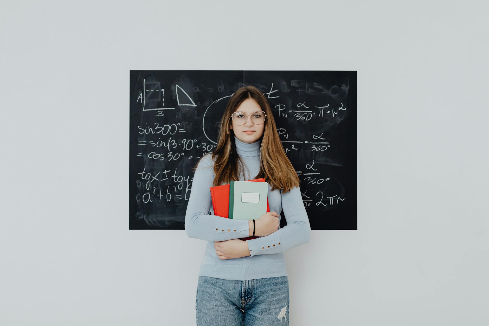 teenage girl standing in front of the blackboard holding notebooks
