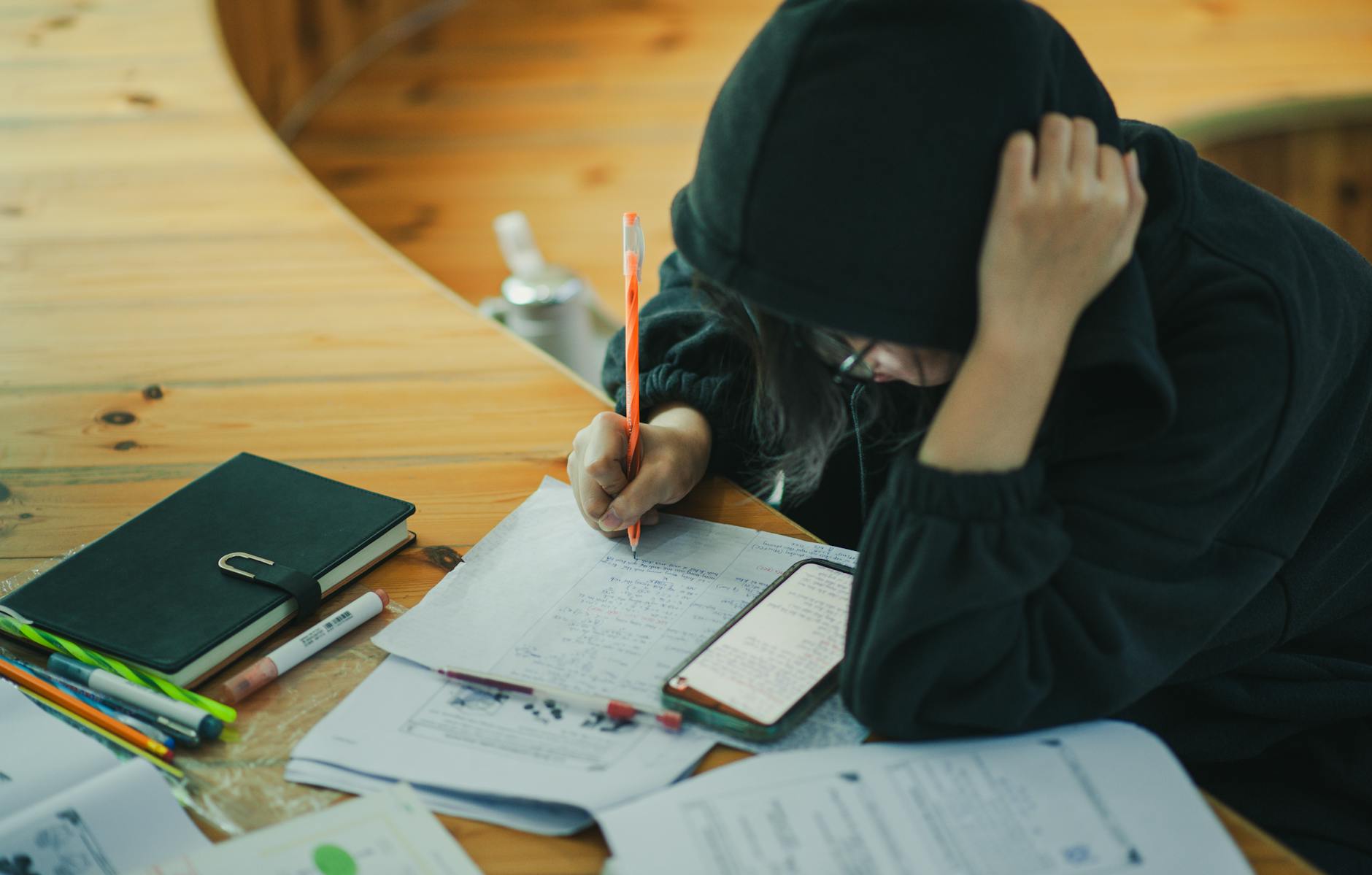 person wearing hoodie writing in notebook